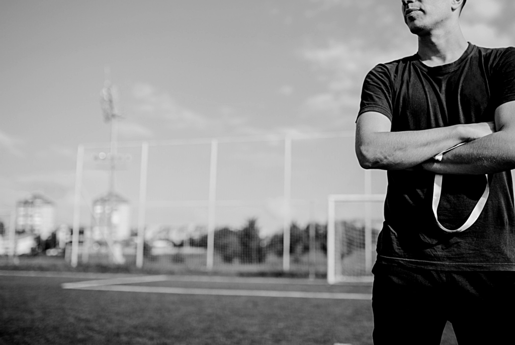 Un entrenador de fútbol de brazos cruzados observando el cmapo
