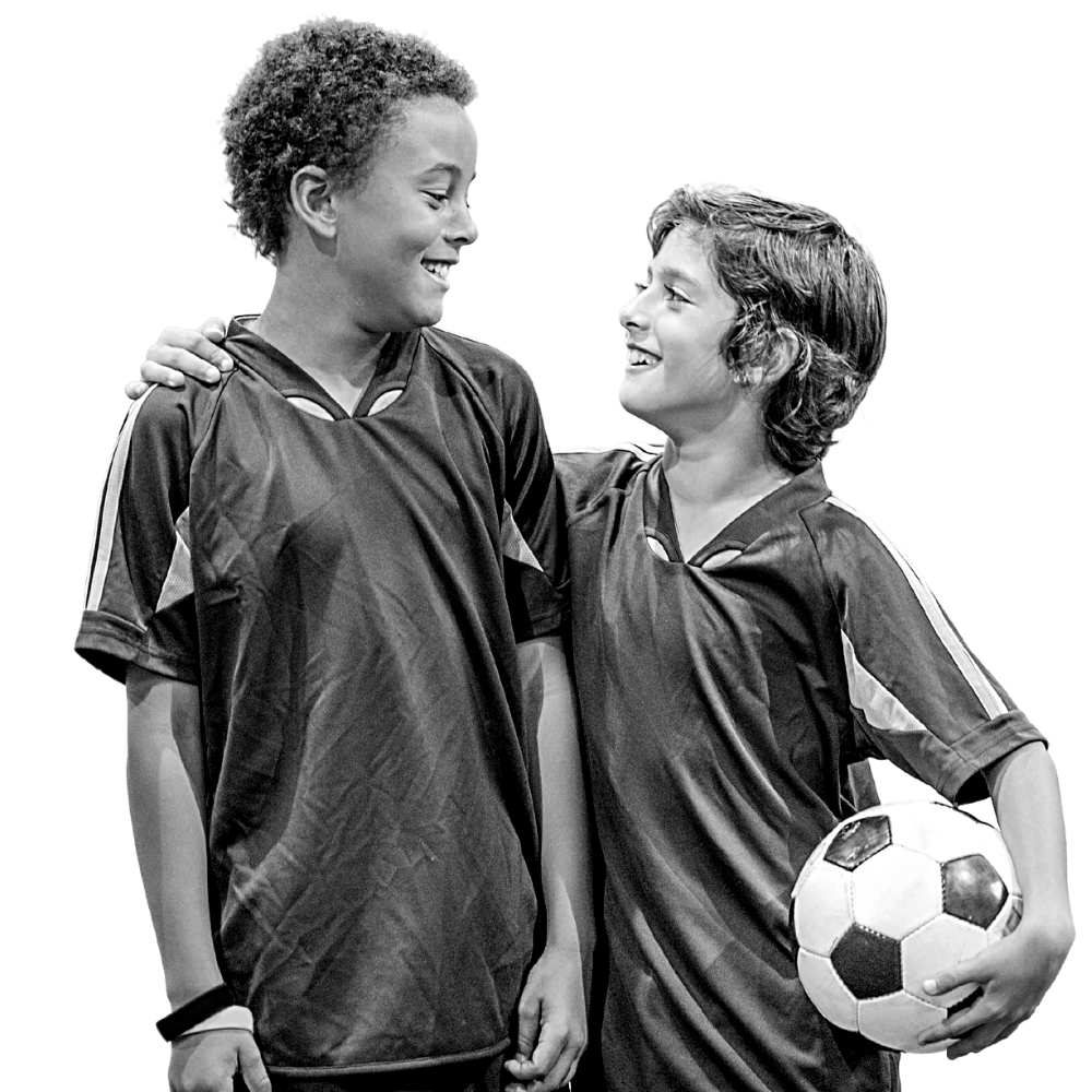 Dos chicos se miran sonrientes mientras uno de ellos sostiene un balón de fútbol