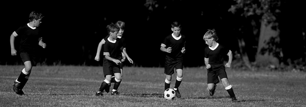 Cinco niños jugando a fútbol persiguen una pelota